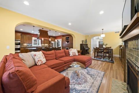 A cozy open-concept living area with a red sectional sofa, wooden dining table, and a kitchen with modern appliances.