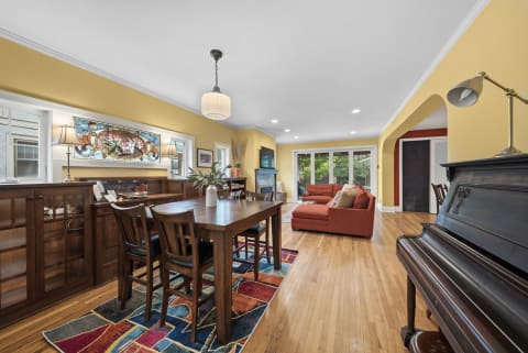 A cozy dining and living area featuring warm walls, a wooden table, an orange sofa, and a black piano.
