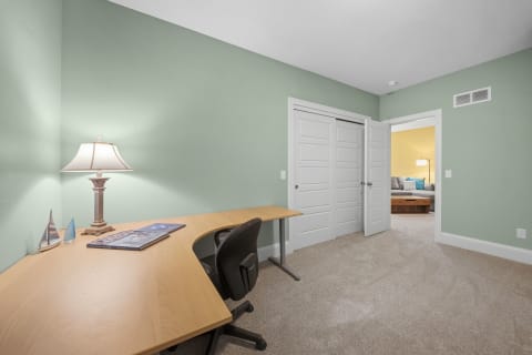 A spacious work-from-anywhere desk with sage-green walls and soft lighting, leading to a cozy lounge area.
