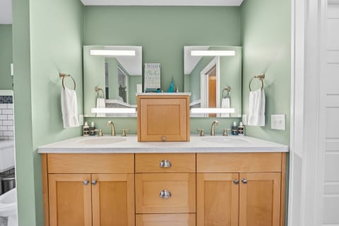 A serene bathroom featuring mint green walls, dual wooden vanities, and gold fixtures with fresh towels.