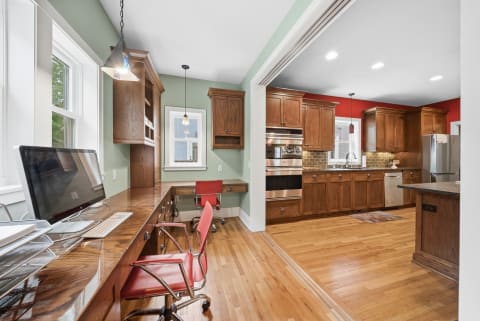 Bright open-plan kitchen with a workspace featuring wooden cabinets and a modern desk area.