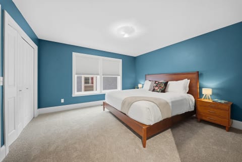 A serene bedroom featuring blue walls, a plush bed with white linens, and a warm wood nightstand.