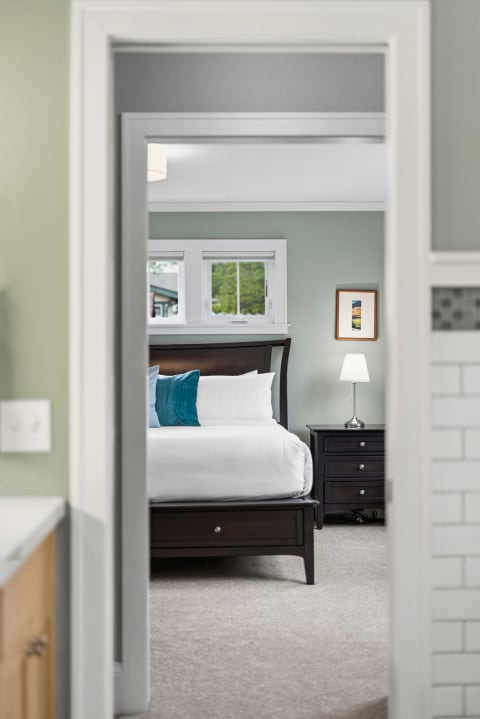 A serene bedroom with a large bed, turquoise pillow, and modern bedside lamp, viewed through a doorway.