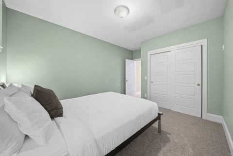 A peaceful bedroom featuring sage-green walls, a bed with white linens, and soft carpeting.
