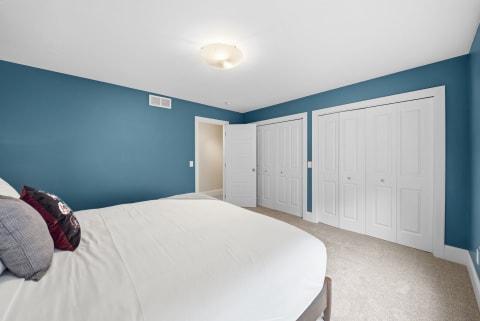 A serene bedroom with teal walls, a white bed, and ample closet space.