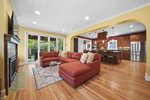 A cozy living room with a red sectional sofa and a kitchen in the background, showcasing wooden cabinets and modern appliances.