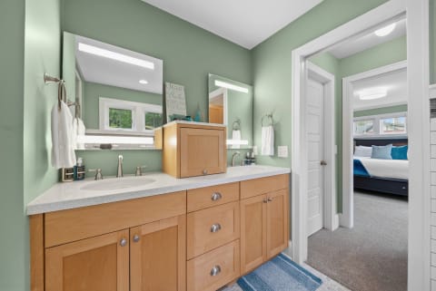 A tranquil bathroom featuring mint green walls, a wooden double vanity, and a doorway leading to a cozy bedroom.