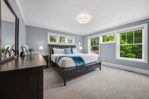 Elegant bedroom with blue-gray walls, luxurious bedding, and bright green views outside the windows.