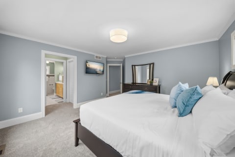 A serene bedroom featuring a king-sized bed with white linens and blue pillows, soft blue walls, and an ensuite bathroom.