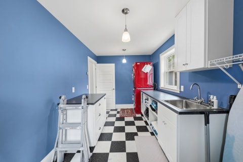 A bright laundry room featuring blue walls, a red refrigerator, and checkered flooring.