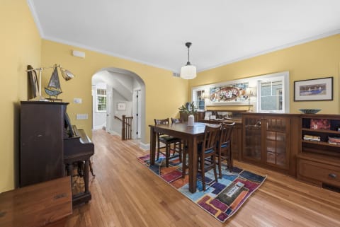 A cozy dining space with yellow walls, wooden furniture, and a colorful rug.