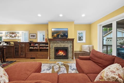 A warm and inviting living room with a rust-colored sectional sofa, a fireplace, and large windows letting in natural light.