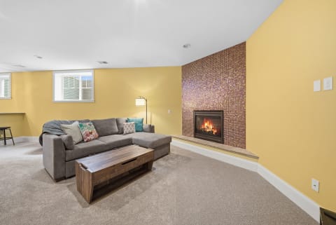 A comfortable living room featuring a sectional sofa, a vibrant fireplace, and sunny yellow walls.