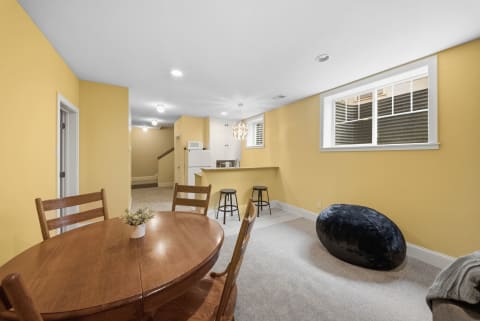 An open-plan living area with yellow walls, a wooden dining table, black stools at a kitchenette, and a large bean bag chair.