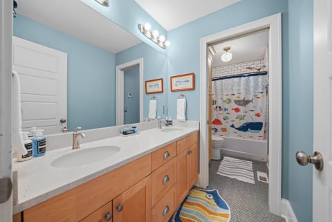 A cheerful bathroom featuring ocean-themed decor with a double sink vanity, colorful fish shower curtain, and playful bath mats.