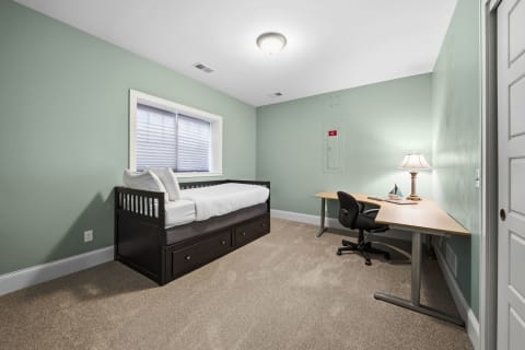 A serene bedroom featuring mint green walls, a daybed with storage, and a desk workspace.
