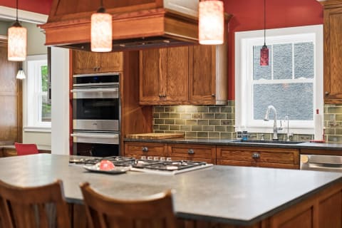 Modern kitchen with wooden cabinetry, pendant lights, and stainless steel appliances.