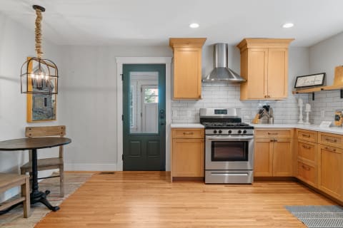 A warm, modern kitchen with wooden cabinets, stainless steel appliances, and a round table with chairs.