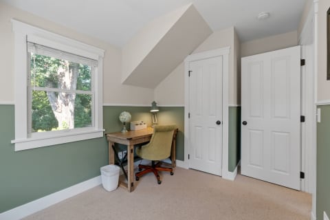 A home office featuring a wooden desk, chair, globe, and view of a tree outside.