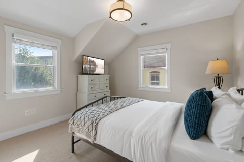 Cozy bedroom featuring a black metal bed, white linens, and a blue decorative pillow with a flat-screen TV and dresser.