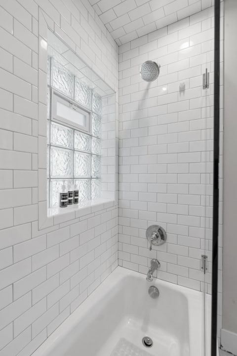 A clean and modern bathroom shower with white tiles and a glass block window.