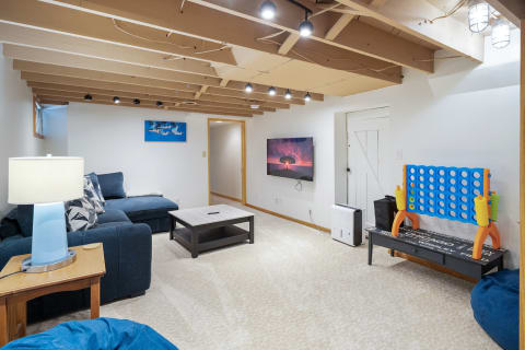 Cozy basement with sectional sofa, flat-screen TV, and a Connect Four game set.
