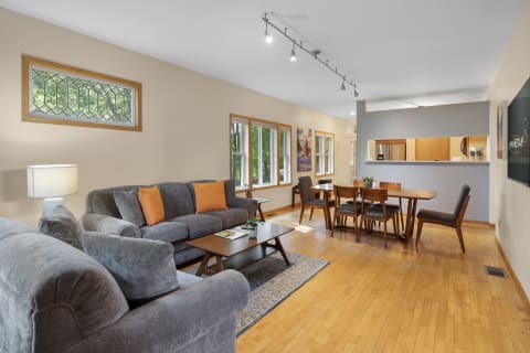 A stylish living room with gray sofas, wooden furniture, and large windows showcasing greenery.