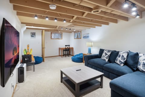 A cozy finished basement with a blue sectional sofa, a flat-screen TV, and decorative toys.