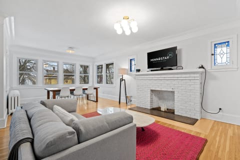 Cozy living room featuring gray sectional sofa, white brick fireplace, and vibrant pink rug.