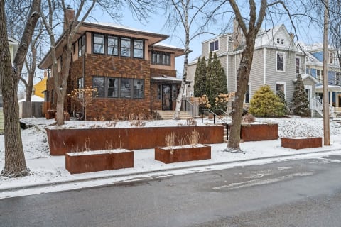 Winter scene of a brown brick house with snow and rust-colored planters.