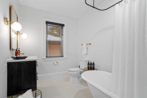 A spacious modern bathroom featuring a sleek black sink cabinet, a freestanding white bathtub, and elegant lighting.