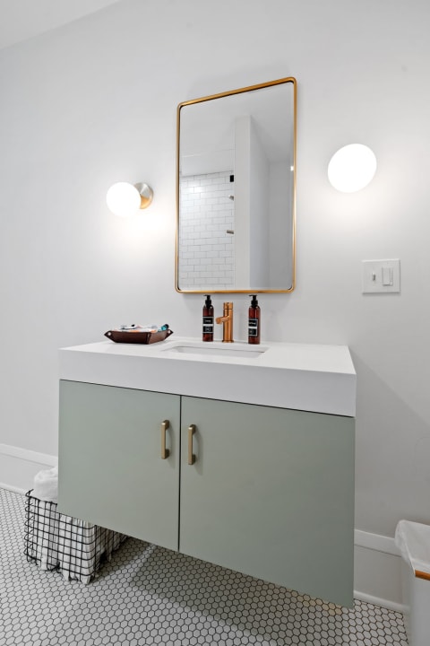 Contemporary bathroom vanity with green cabinetry, white countertop, and a round mirror.