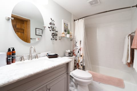 A modern bathroom with marble countertop, round mirror, and floral shower curtain.