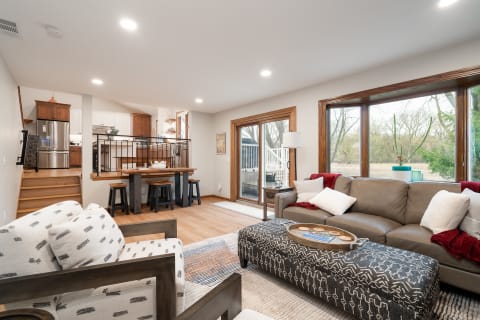 An inviting living room featuring a gray leather sofa, an ottoman, and a view of the kitchen and outdoors.