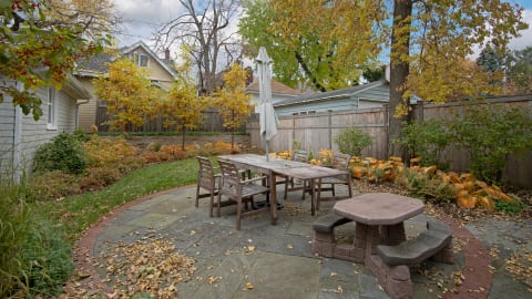 Outdoor dining area with wooden table and chairs surrounded by colorful autumn leaves.