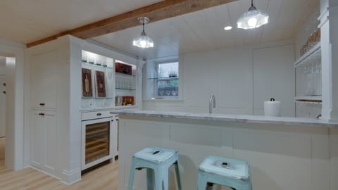 A modern kitchen with marble countertops, aqua stools, and white cabinetry adorned with glass shelves.