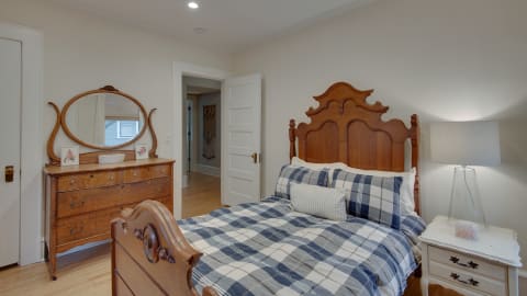 A warm and inviting bedroom with a wooden bed, plaid bedding, and vintage dresser with a mirror.