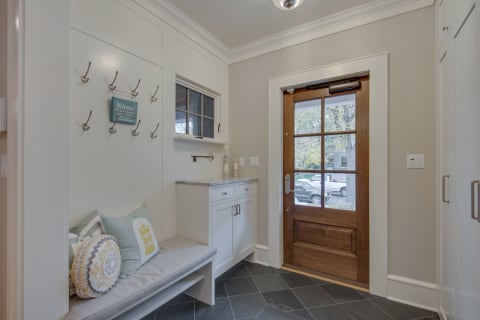 A stylish entryway showcasing a wooden door, built-in seating with decorative pillows, and coat hooks on the wall.