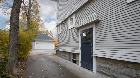 Gray house with a blue entrance door and stone base, surrounded by trees in fall colors.