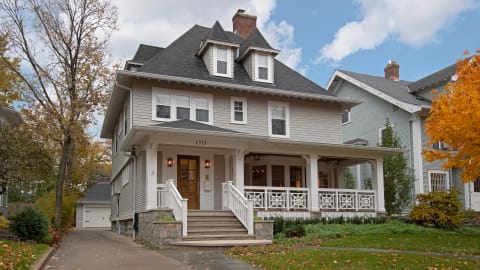Classic two-story house featuring detailed architecture, spacious front porch, and beautiful autumn surroundings.