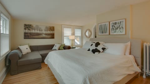 A well-designed bedroom with a large bed, cozy couch, artwork, and natural light.