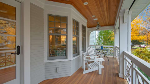 A cozy covered porch featuring white Adirondack chairs, a small table, and autumn views outside.