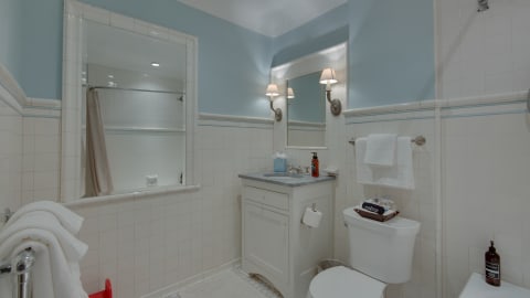 An elegant bathroom featuring soft blue walls, white fixtures, and thoughtful amenities.
