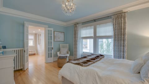Elegant bedroom with blue walls, crystal chandelier, and cozy white bed beneath soft linens.