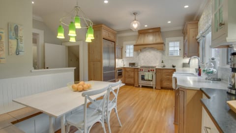 A modern and stylish gourmet kitchen with wooden cabinetry, stainless steel appliances, and a cozy dining table with a bowl of oranges.