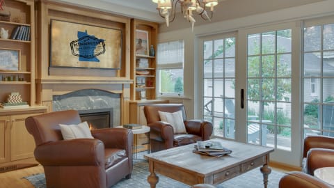 A cozy living room featuring leather armchairs, a fireplace, and large windows with a view of the outdoors.