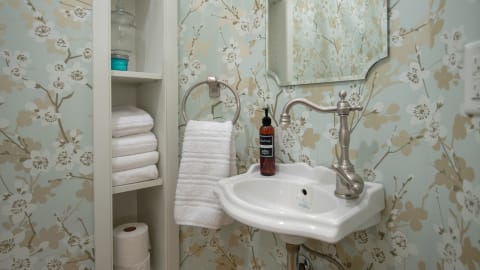 Powder room featuring floral wallpaper, a white sink, and neatly folded towels.