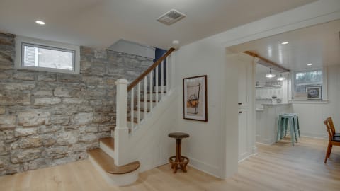 Stylish open-plan living area with a staircase, exposed stone wall, and a glimpse of a modern kitchen.