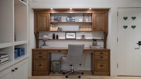 A cozy workspace featuring wood cabinetry, a desk with a globe and books, and a comfortable chair.