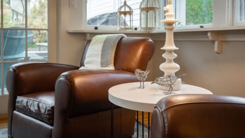 A cozy reading nook with brown leather armchairs, a white side table, and decorative bird sculptures.